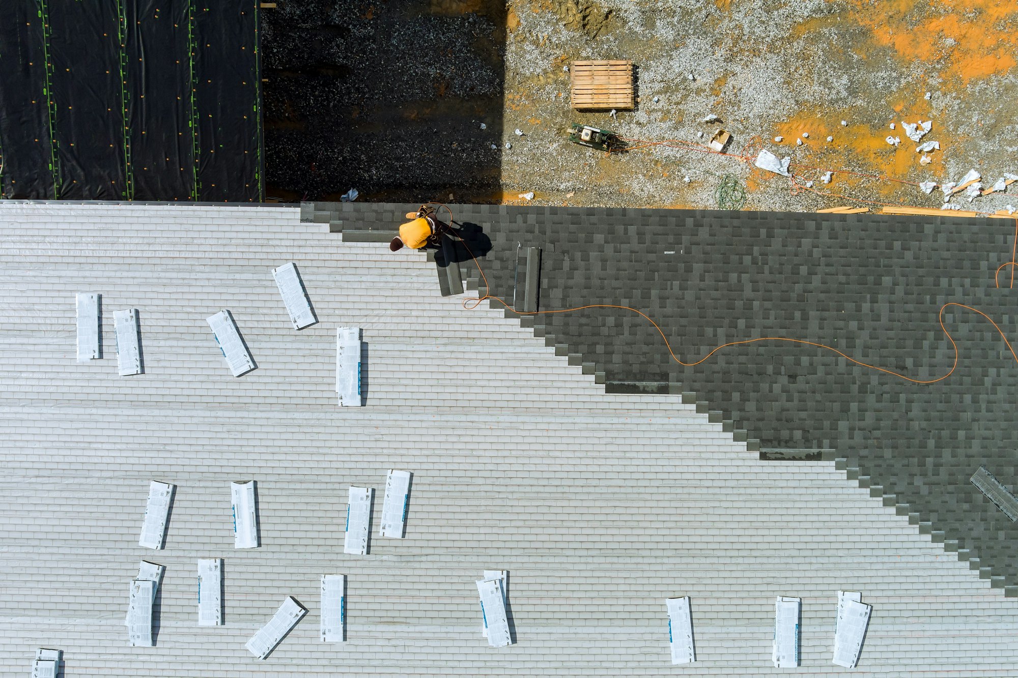 Roofer hands installing asphalt shingles on house construction roof with hammer and nails